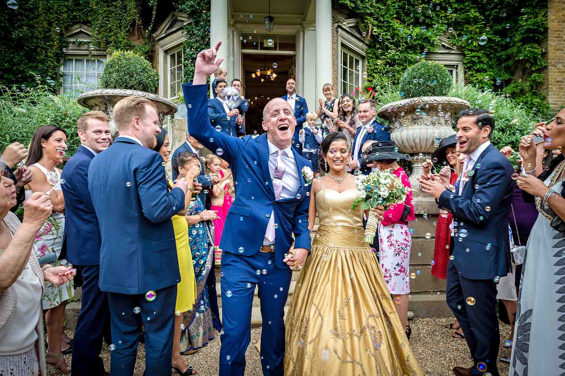 Groom with arm in air after leaving Hampton Court House wedding