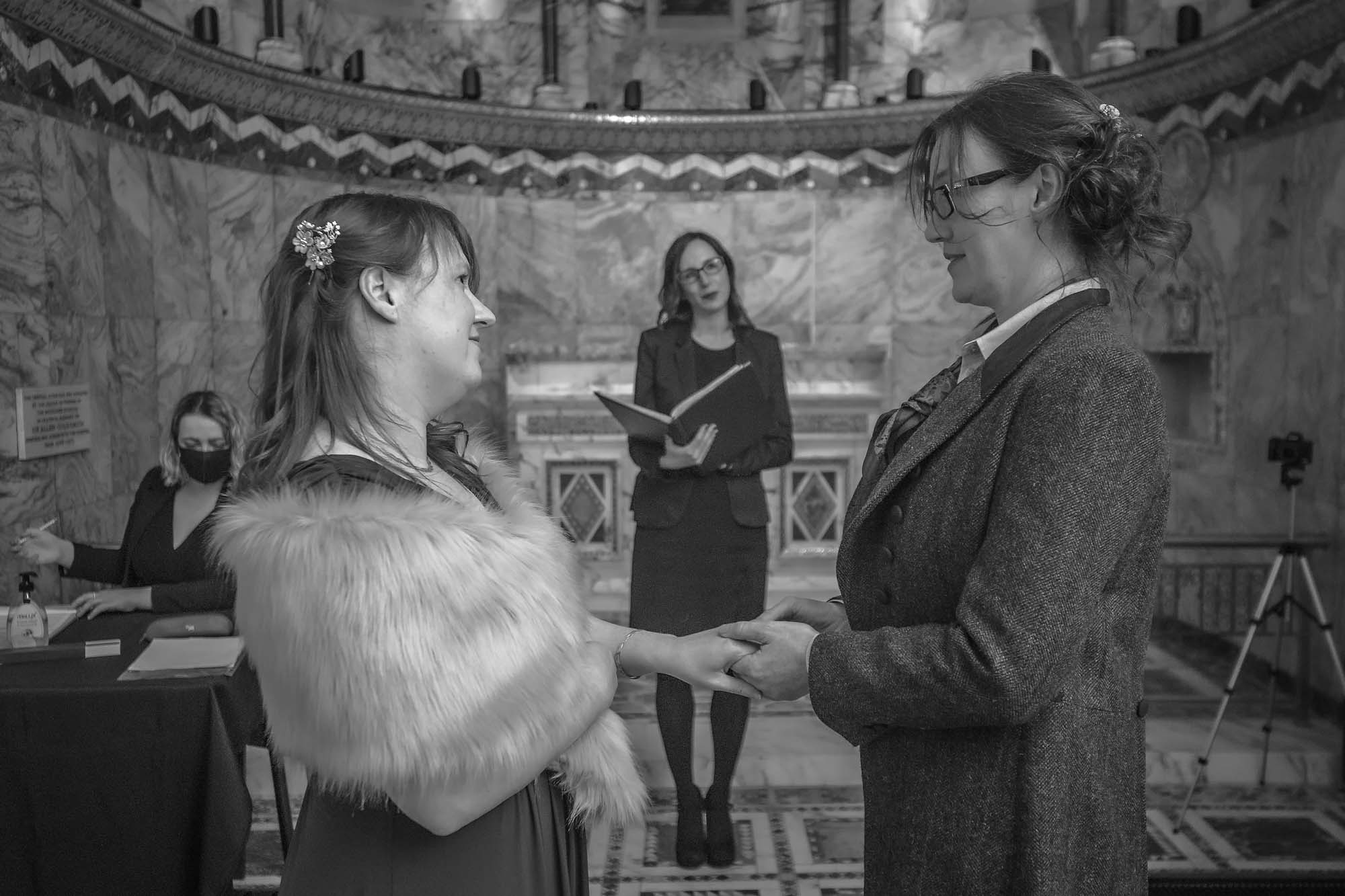 Same-sex couple hold hands during their wedding ceremony at Fitzrovia Chapel, London