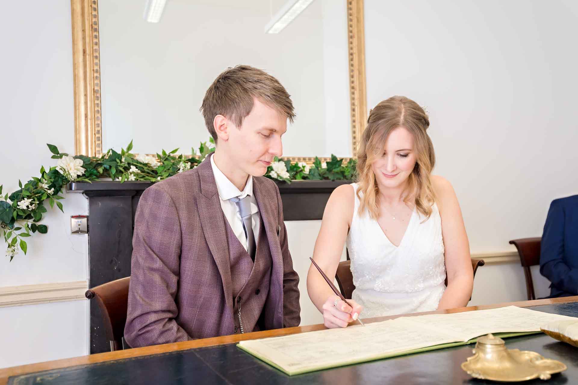 Posed shot of bride signing the register with groom watching at the Old Council House Bristol