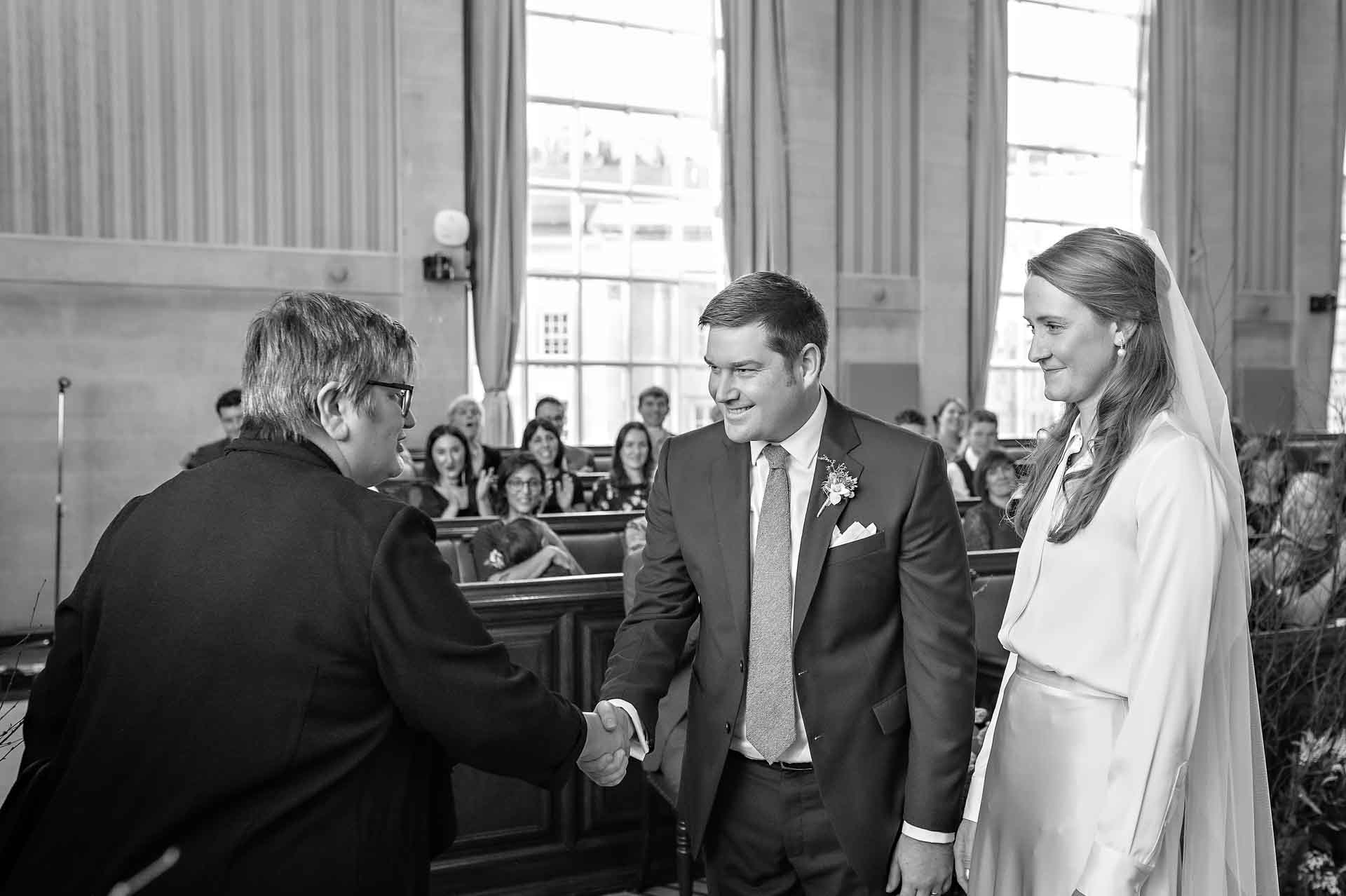 Registrar shakes hand of groom whilst bride watches