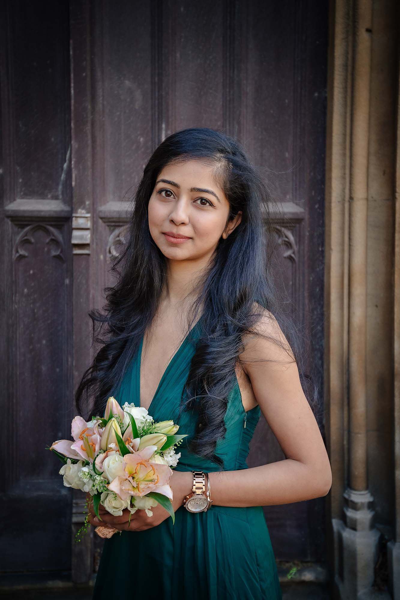A bridesmaid in green poses with her bouquet outside St Luke's Church in Chelsea