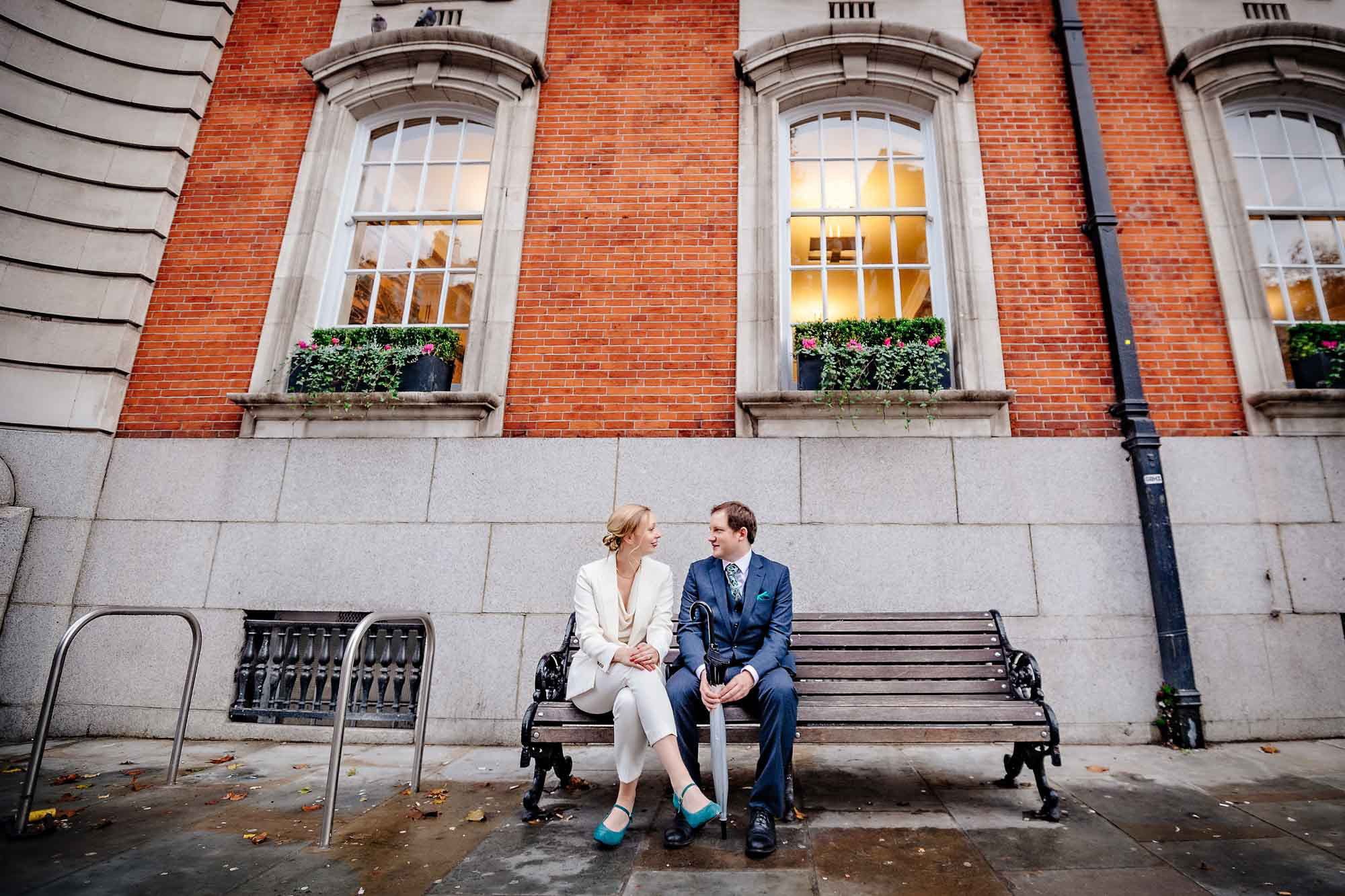 Couple seated on bench outside Chelsea Old Town Hall before wedding