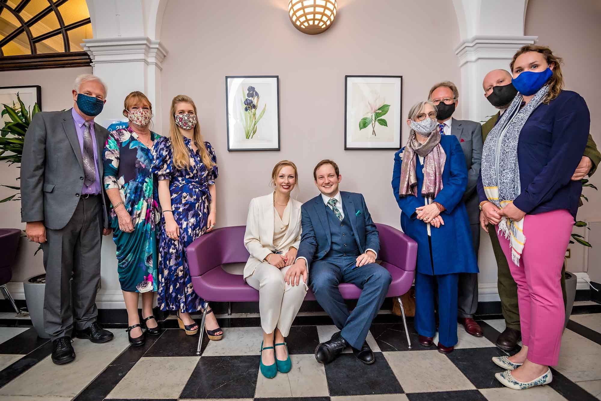 Bride and groom seated with masked guests standing in waiting area at Chelsea Old Town Hall wedding