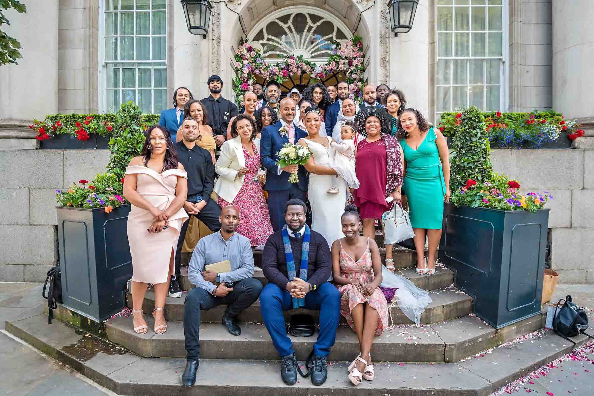 Large group of guests posing with the couple outside Chelsea Old Town Hall