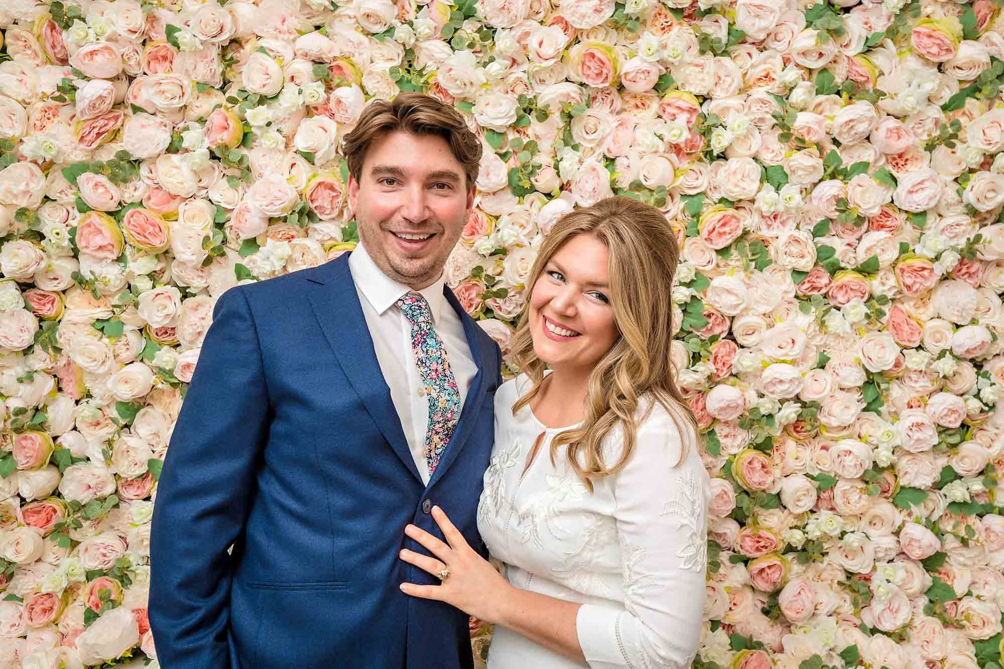 Happy couple posing in front of a wall of roses in Chelsea Old Town Hall