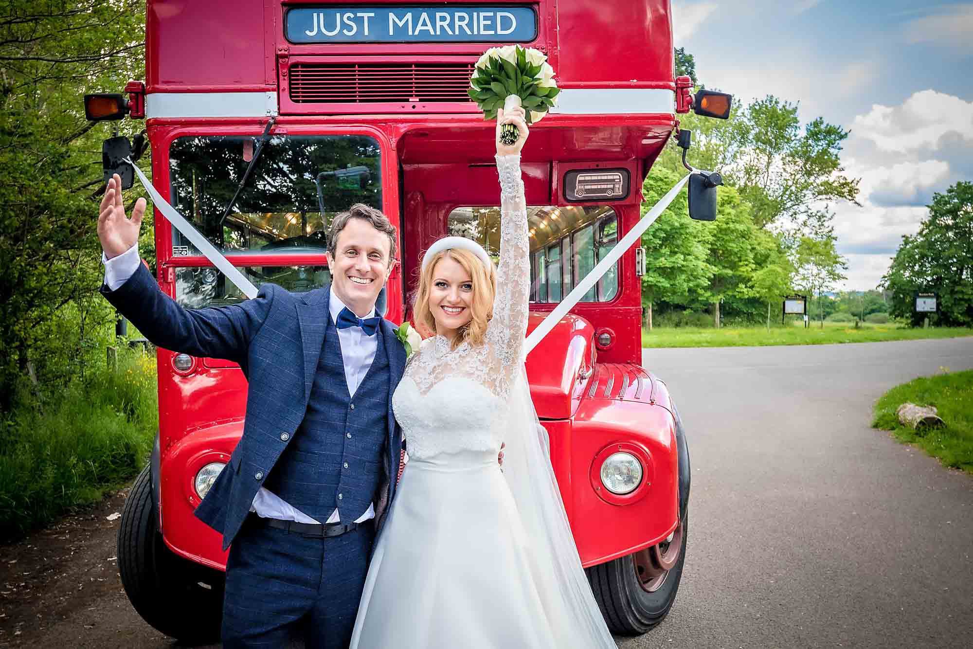 The bride and groom hold their arms in the air, posing in front of a routemaster bus