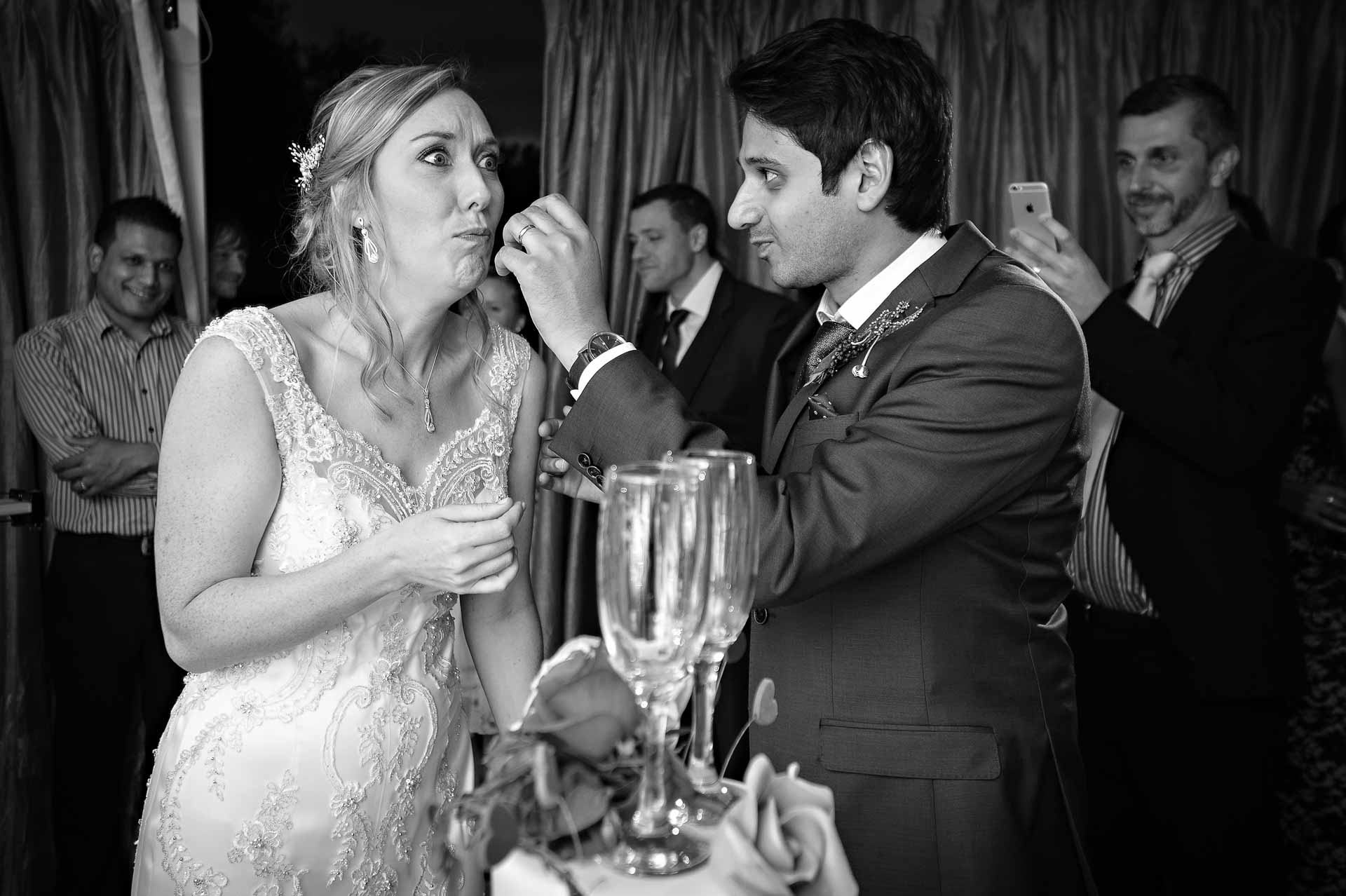 Bride being fed wedding cake by groom pulling funny face