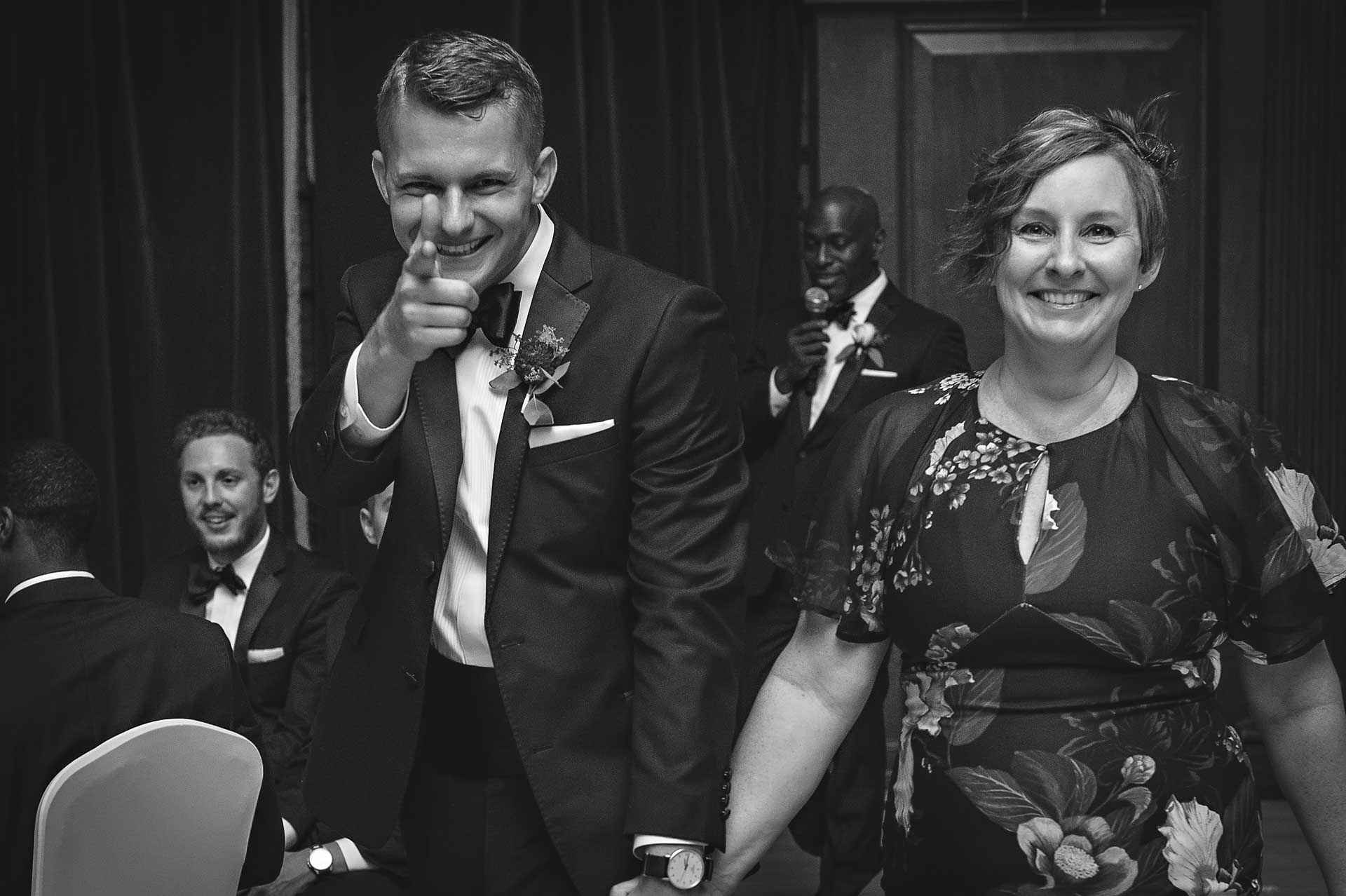 Groom pointing at camera whilst leading mother on to the dance floor