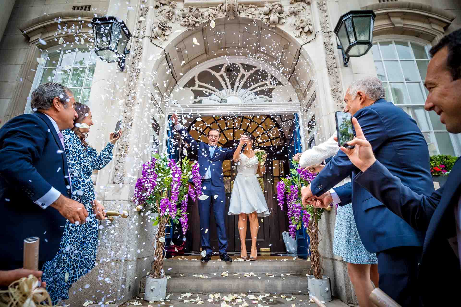 The newly-weds are covered in cofetti on the steps of Chelsea Old Town Hall