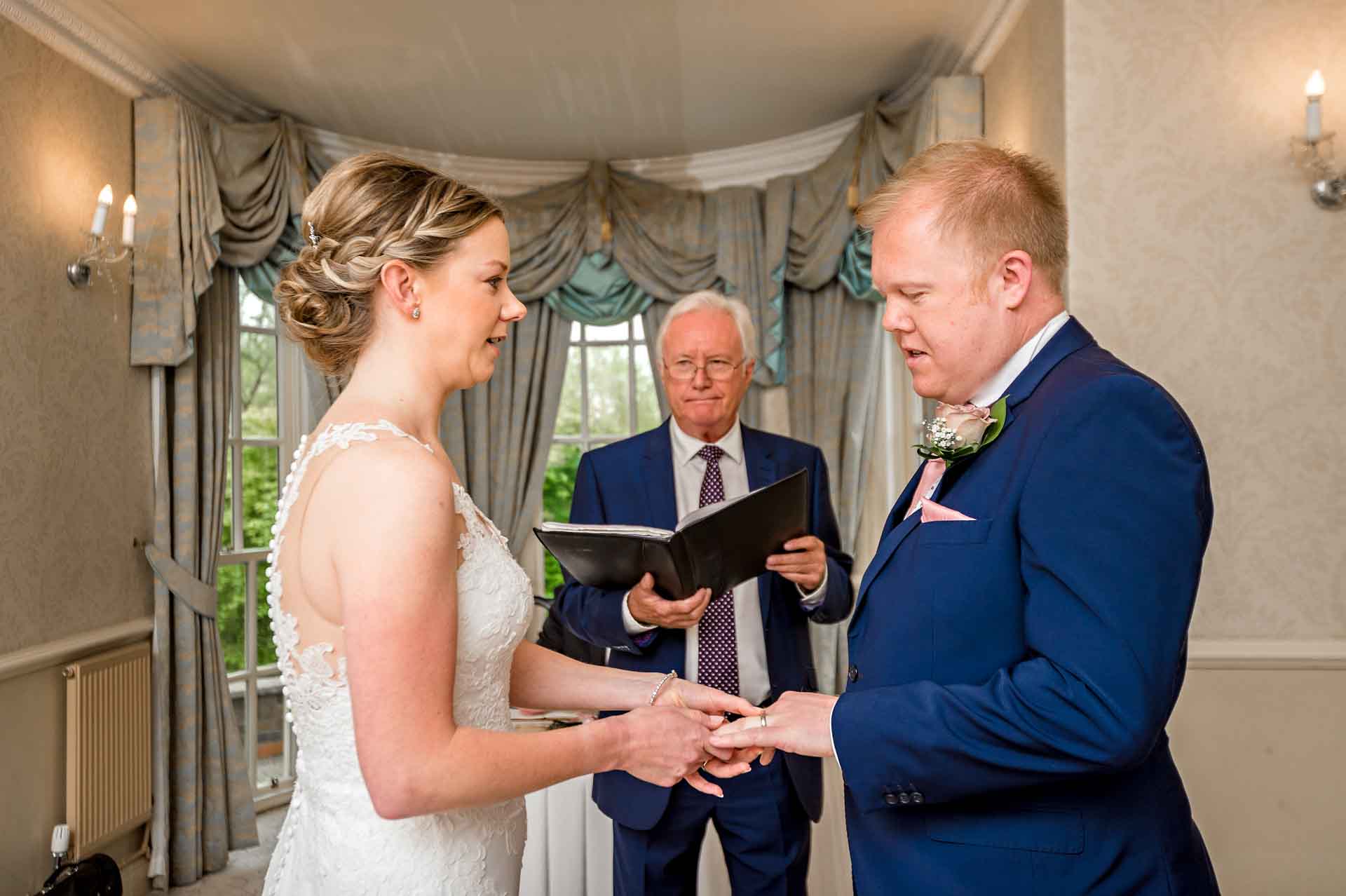 Bride places ring on groom's finger at DeCourceys Manor