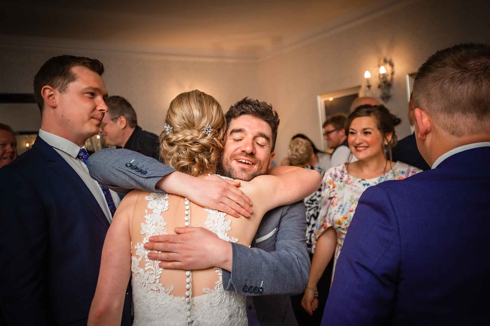 Male guest hugging bride with eyes shut at wedding