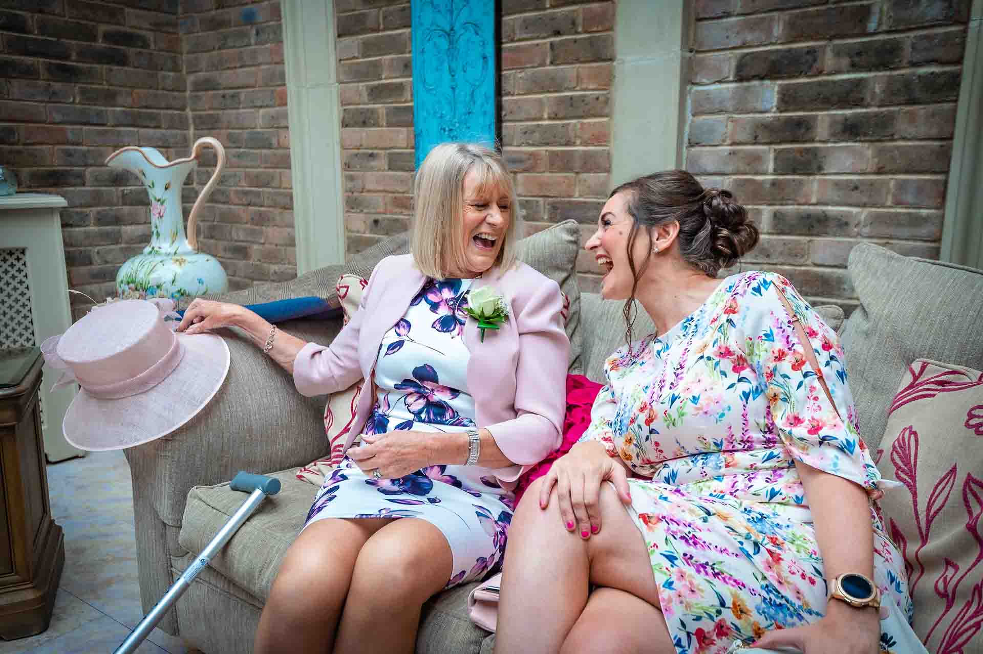 Two female guests laughing on sofa at wedding