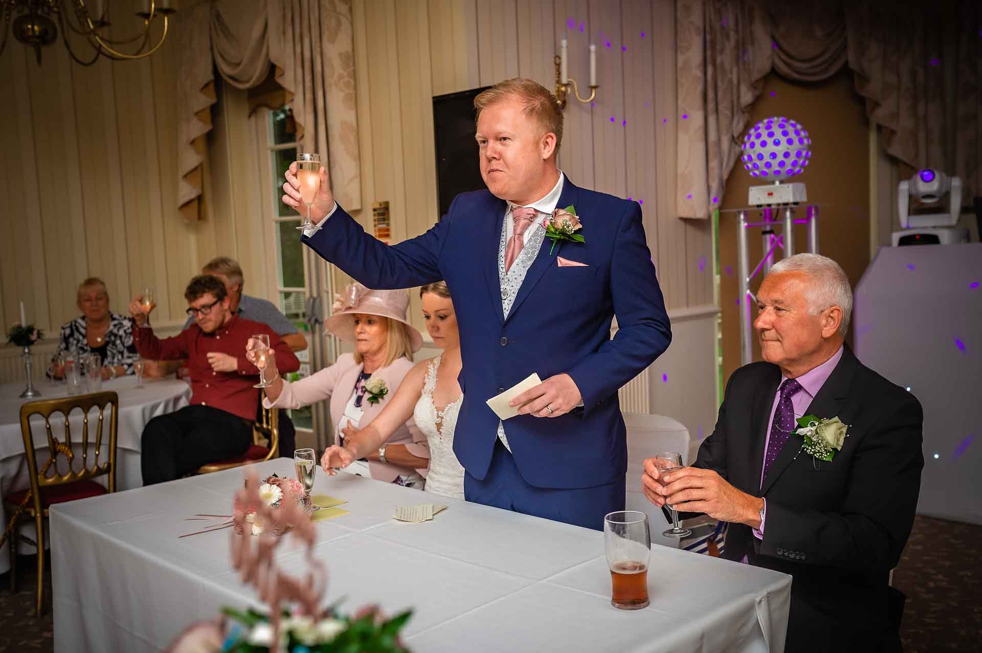 Groom raising glass for toast at wedding near Cardiff