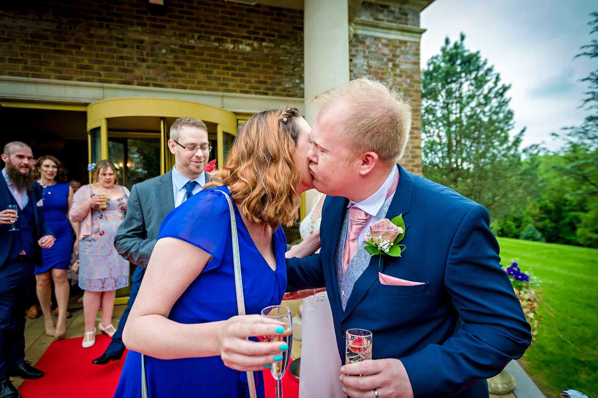 Groom kisses female guest on cheek outside DeCourceys Manor Cardiff