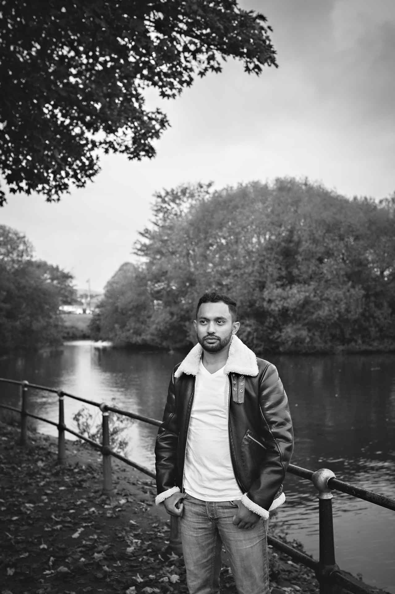 Male with thumbs in pockets looking away from camera next to moat in black and white