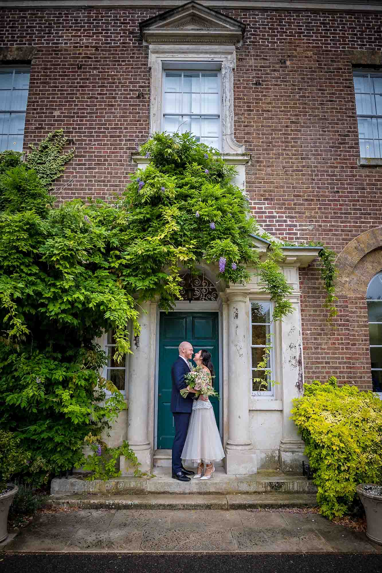 Newly-wedded couple holding each other outside Merton Register Office/Morden Park House
