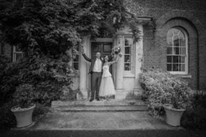 Wedding couple with arms in air outside Morden Park House, Merton