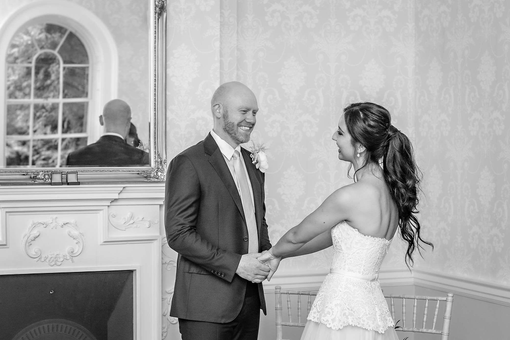 The bride and groom holding hands and smiling in the Sheridan Room at Morden Park House