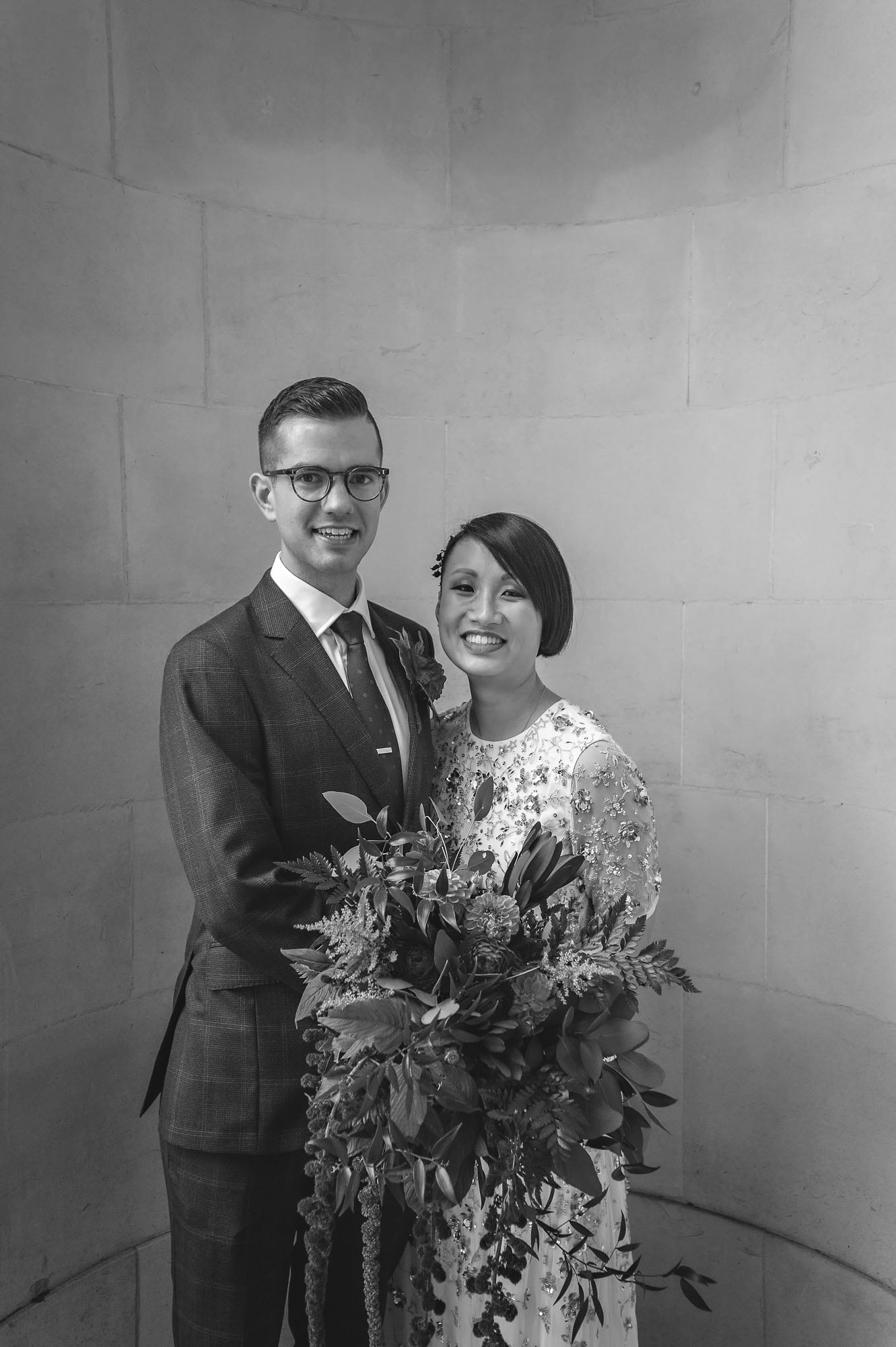 Black and white portrait of a couple with large bouquet posing outside Old Marylebone Town Hall