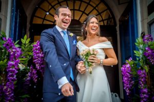 Bride and groom laughing between purple wedding flower display at Chelsea Old Town Hall