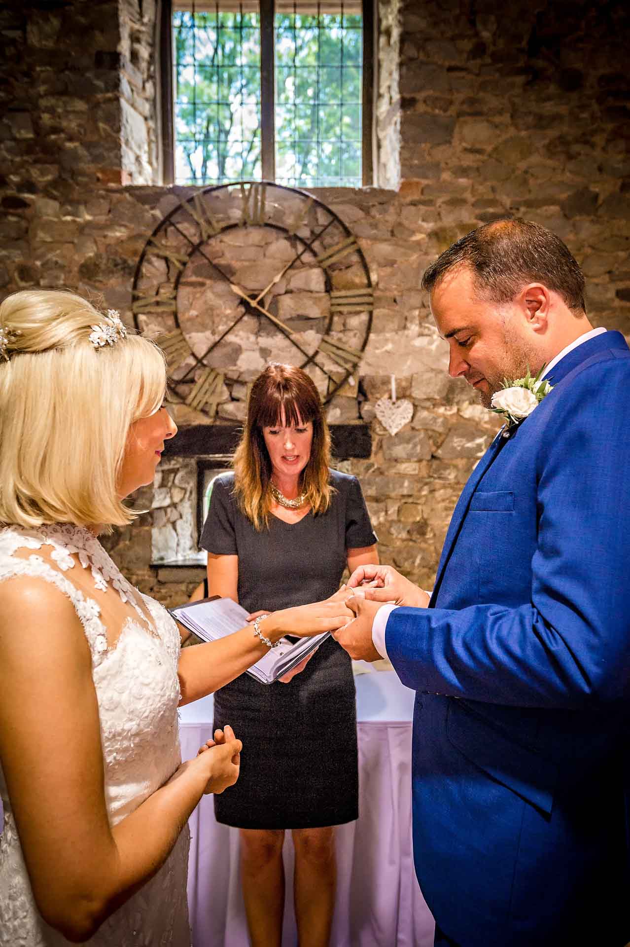 Grrom Placing Ring on Bride's Finger in Old Barn at Pencoed House