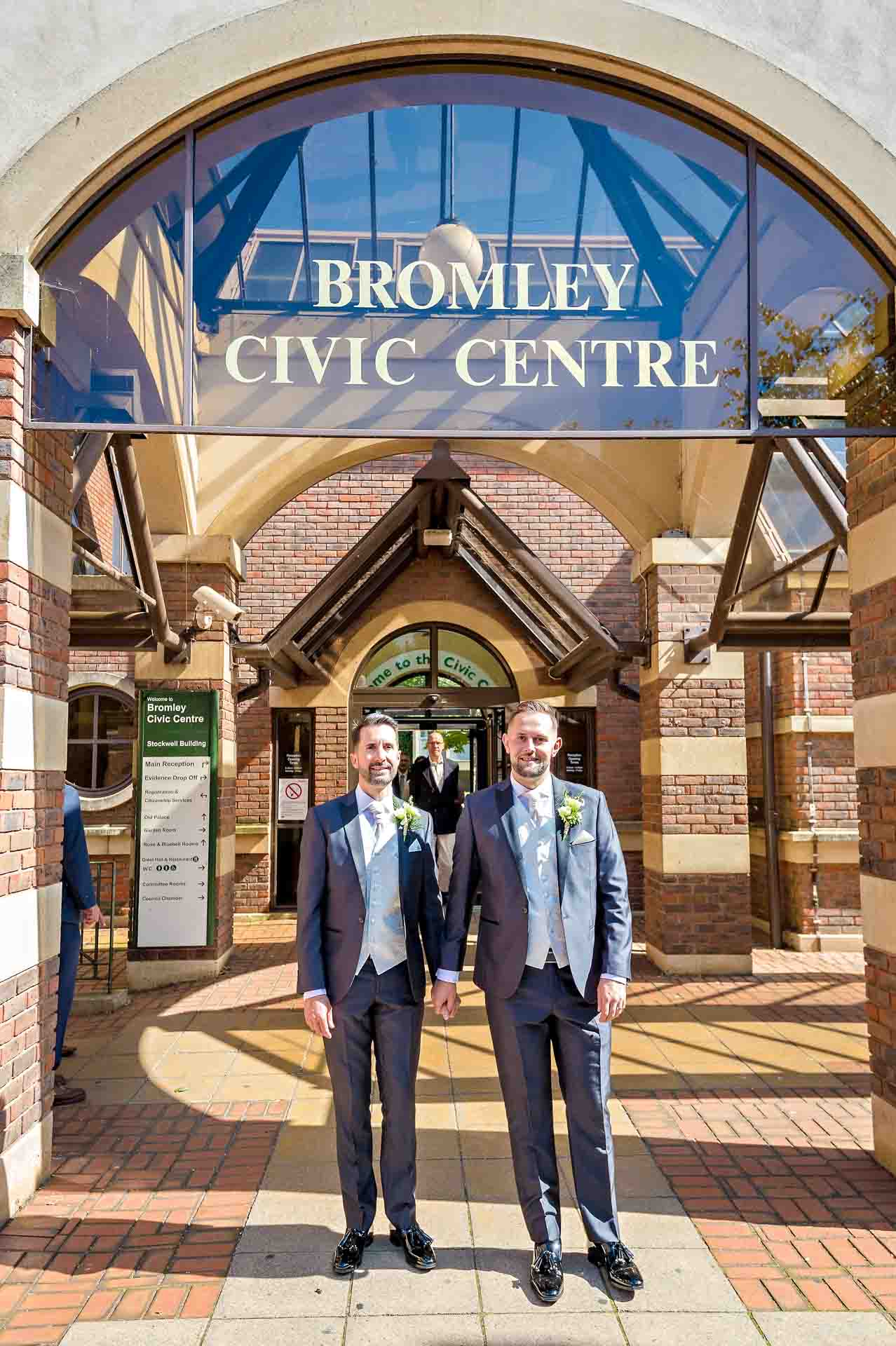 Same-sex wedding grooms standing together in front of Bromley Civic Centre