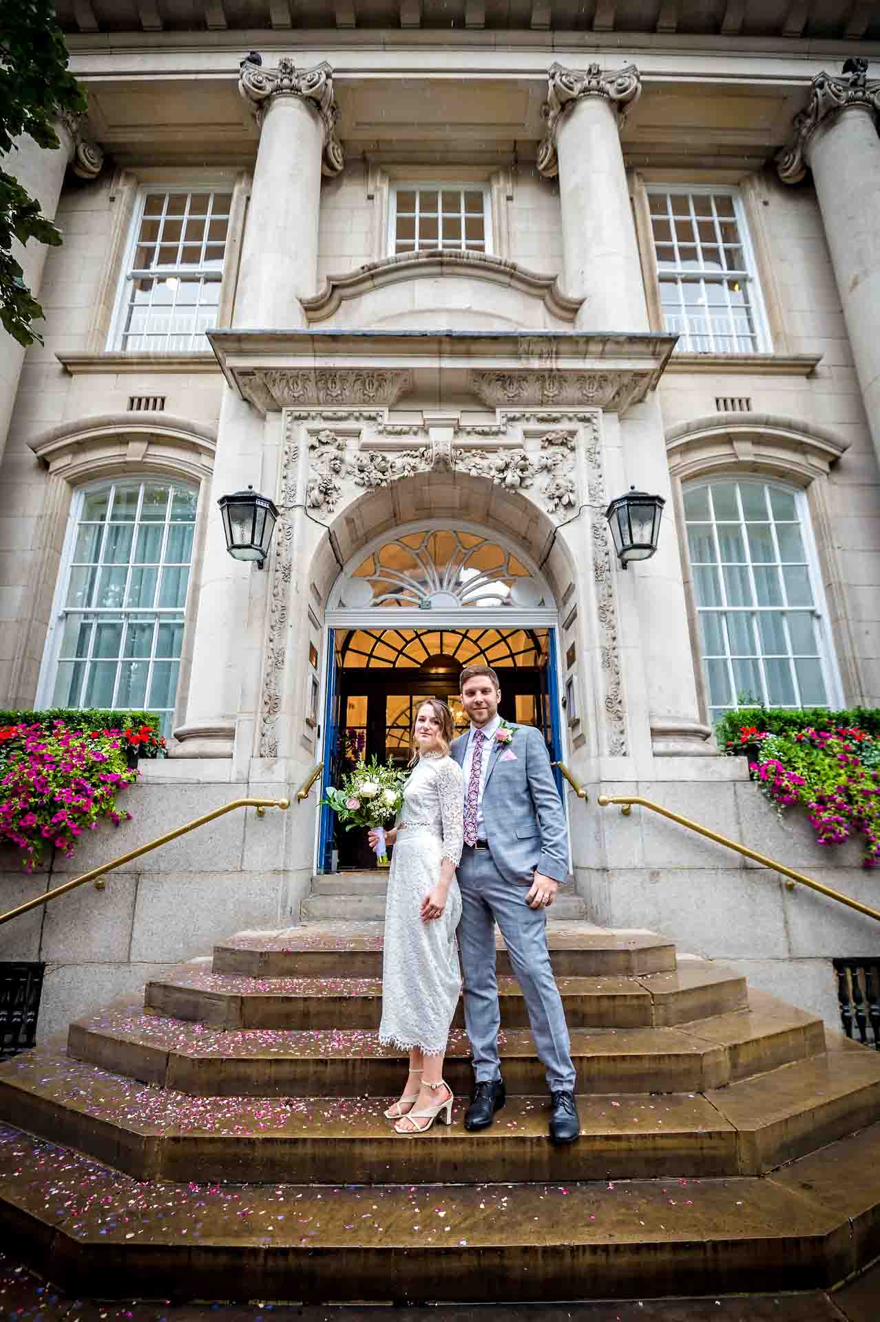Newly married couple standing on wet steps of Chelsea Old Town Hall
