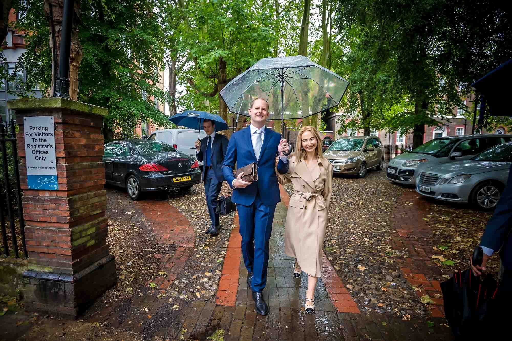 The newlyweds walk down the drive of Southwark Register Office under a clear umbrella
