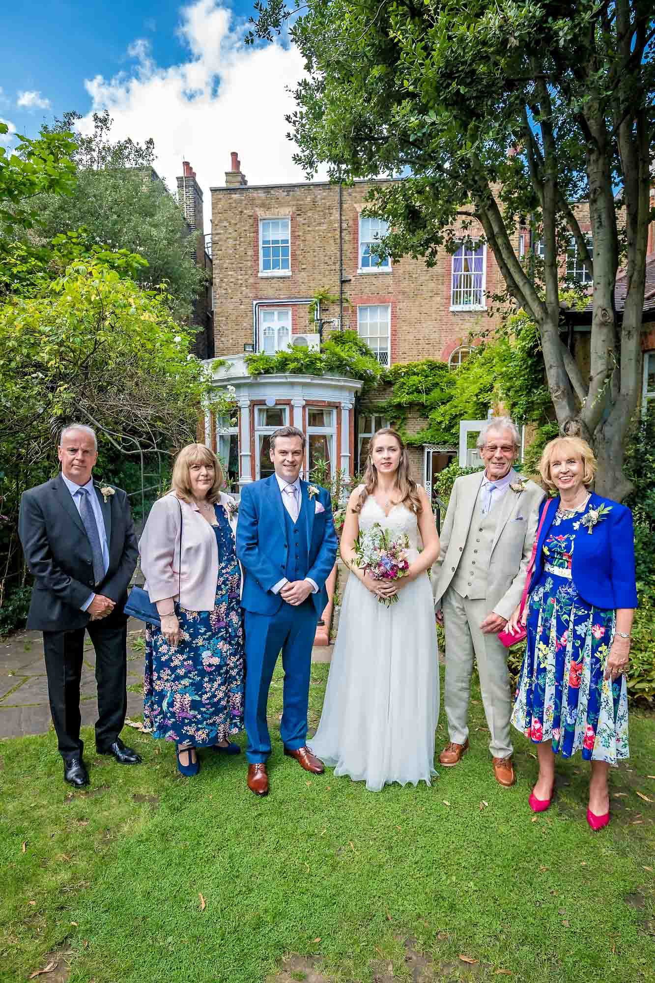 Newlyweds pose with their parents with in the garden of Southwark Register Office with the house in the background