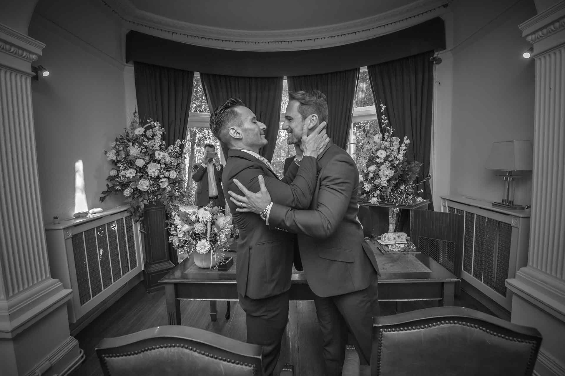 Gay newly-weds holding each other in Garden Room of Southwark Register Office