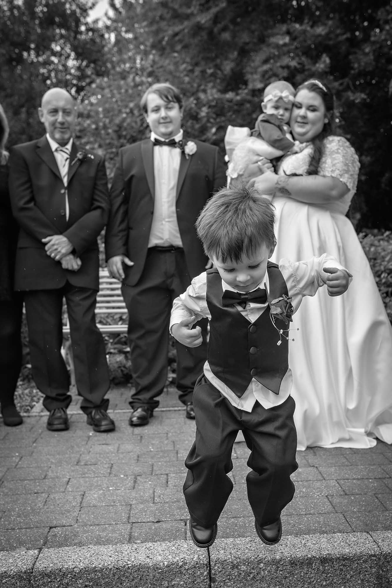 Little boy jumping off step during posed wedding photos in Penallta House