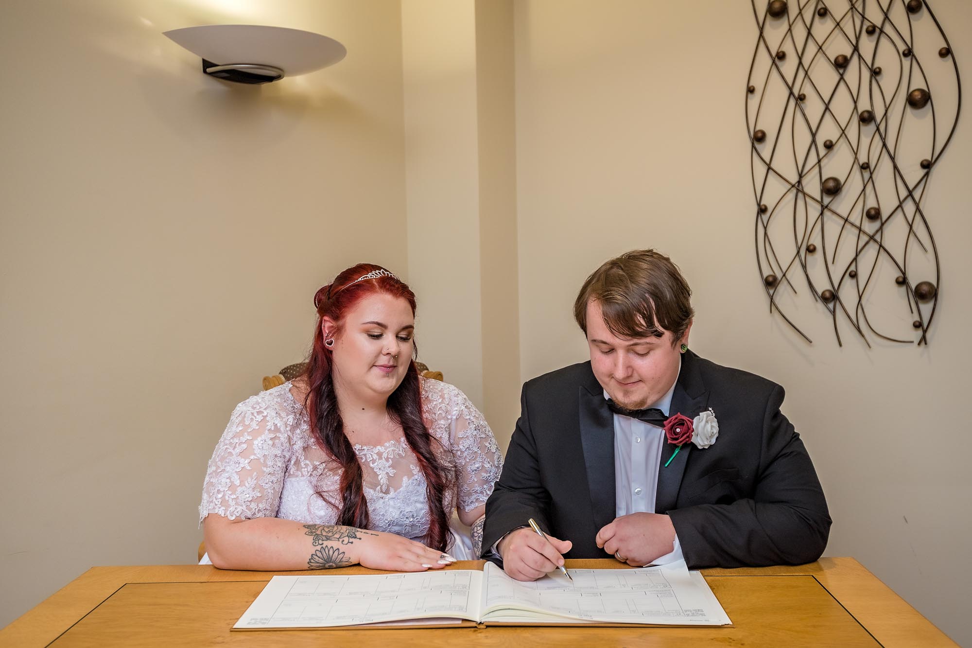 The groom poses signing the register as his bride looks on in Penallta House
