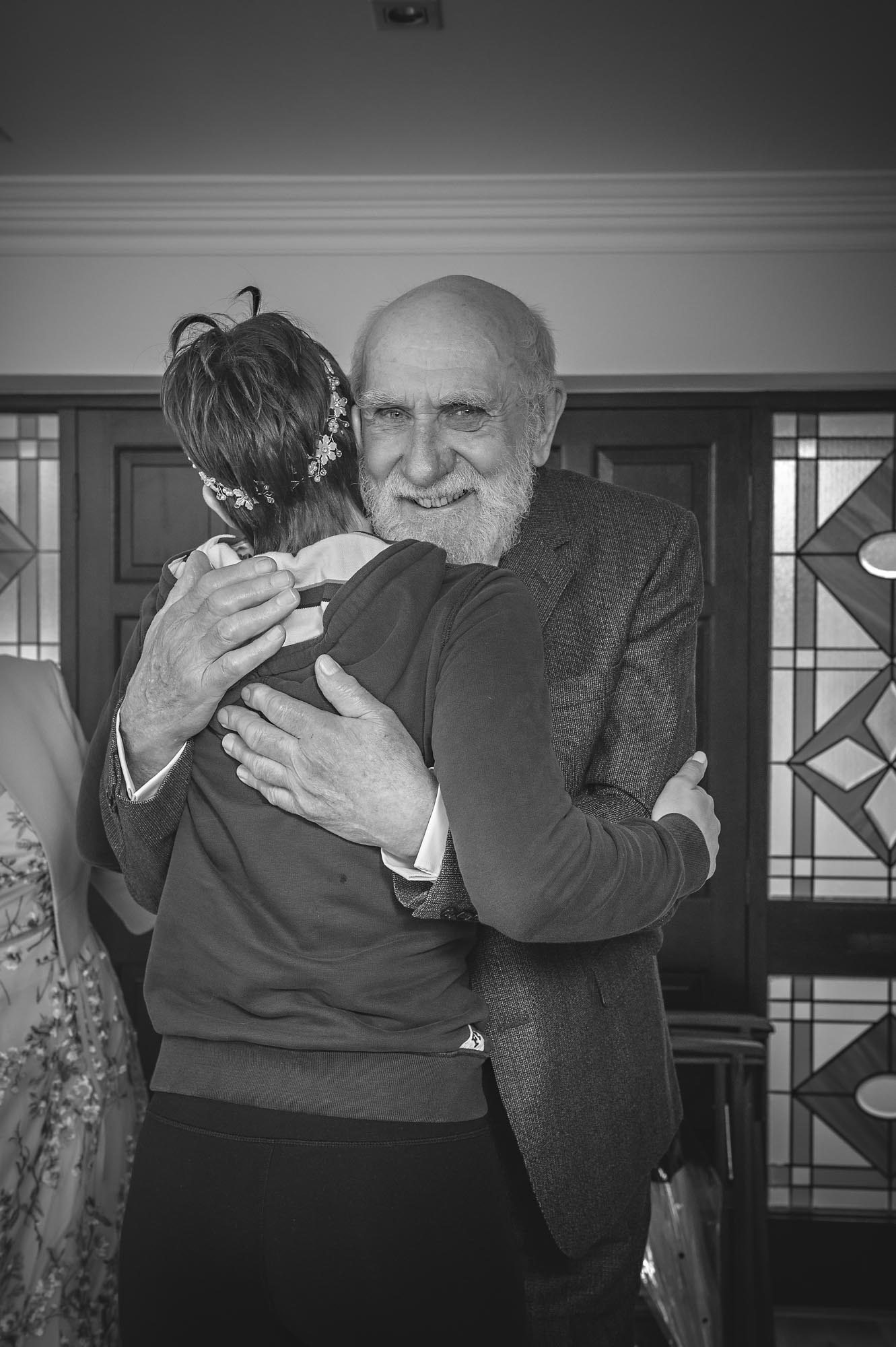 A bearded grandfather hugs the bride and smiles at wedding preparations