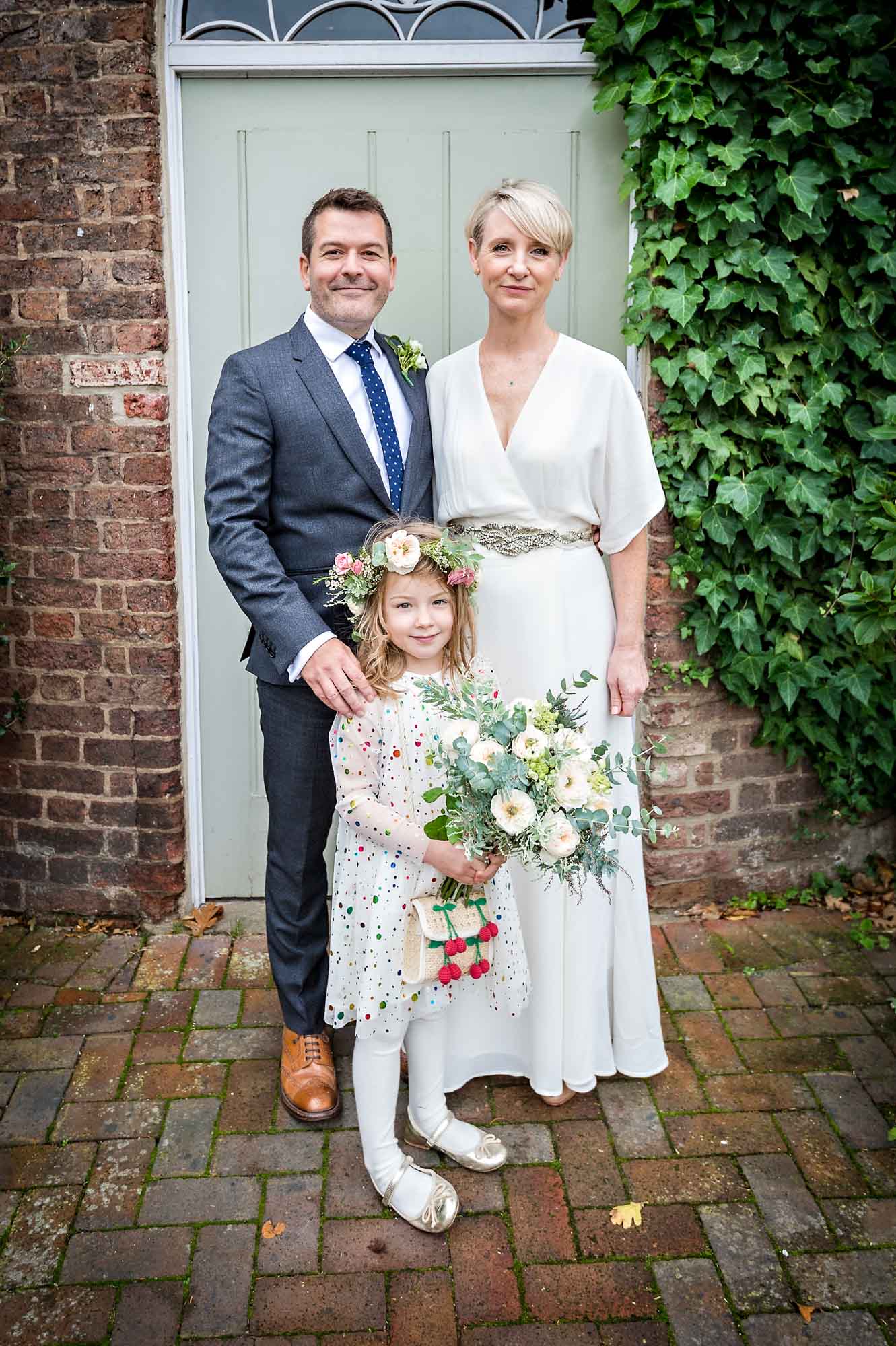 The bride and groom pose with their daughter after wedding at Morden Park House