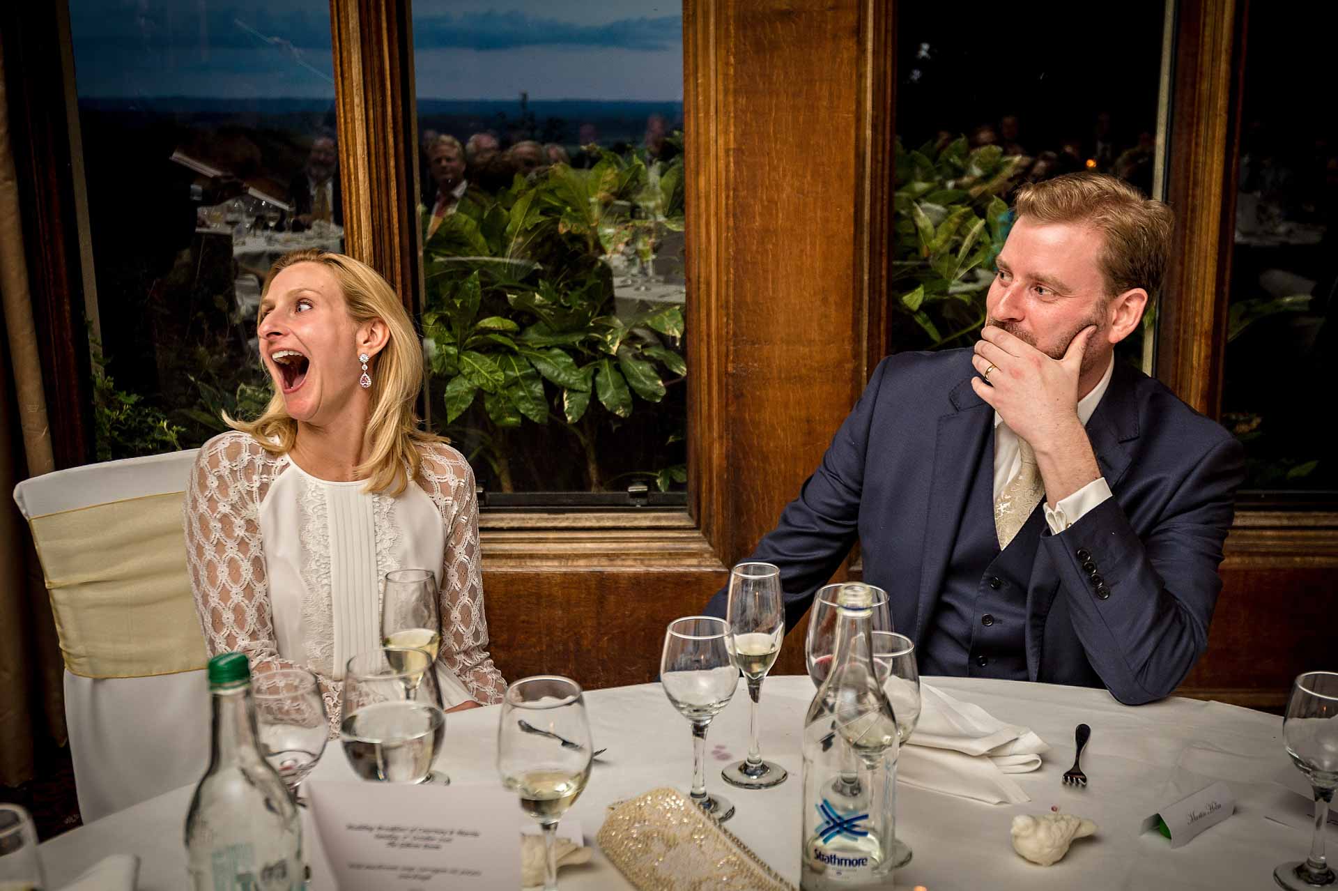 Bride laughing in surprise and groom with hand over mouth during wedding speech in Cardiff