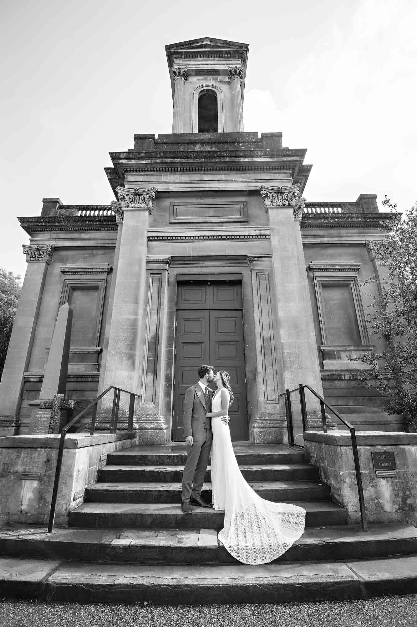 Black and white portrait of newlyweds kissing on steps of the Anglican Chapel at Arnos Vale
