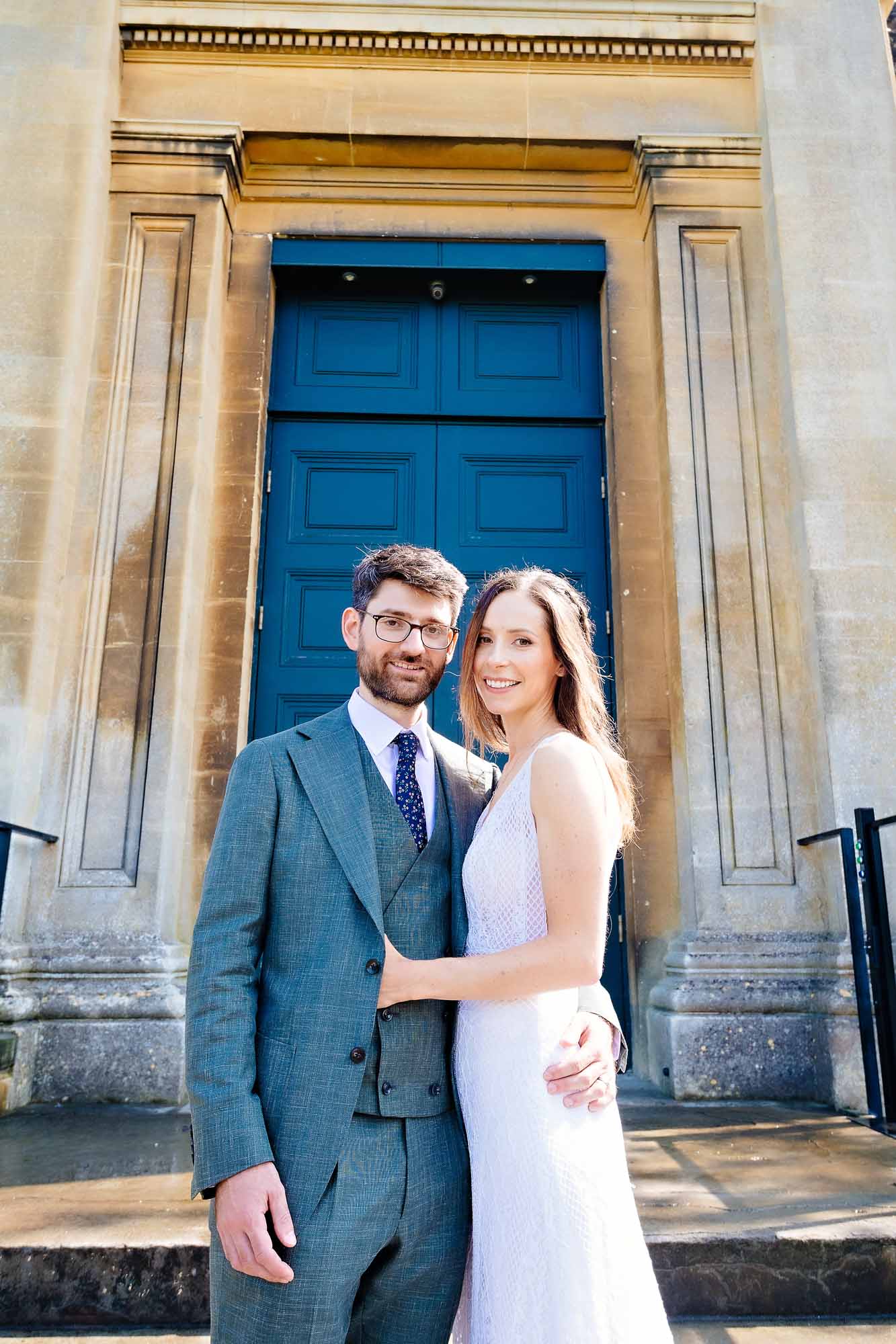 The bride and groom pose in the sun outside the Anglican Chapel at Arnos Vale