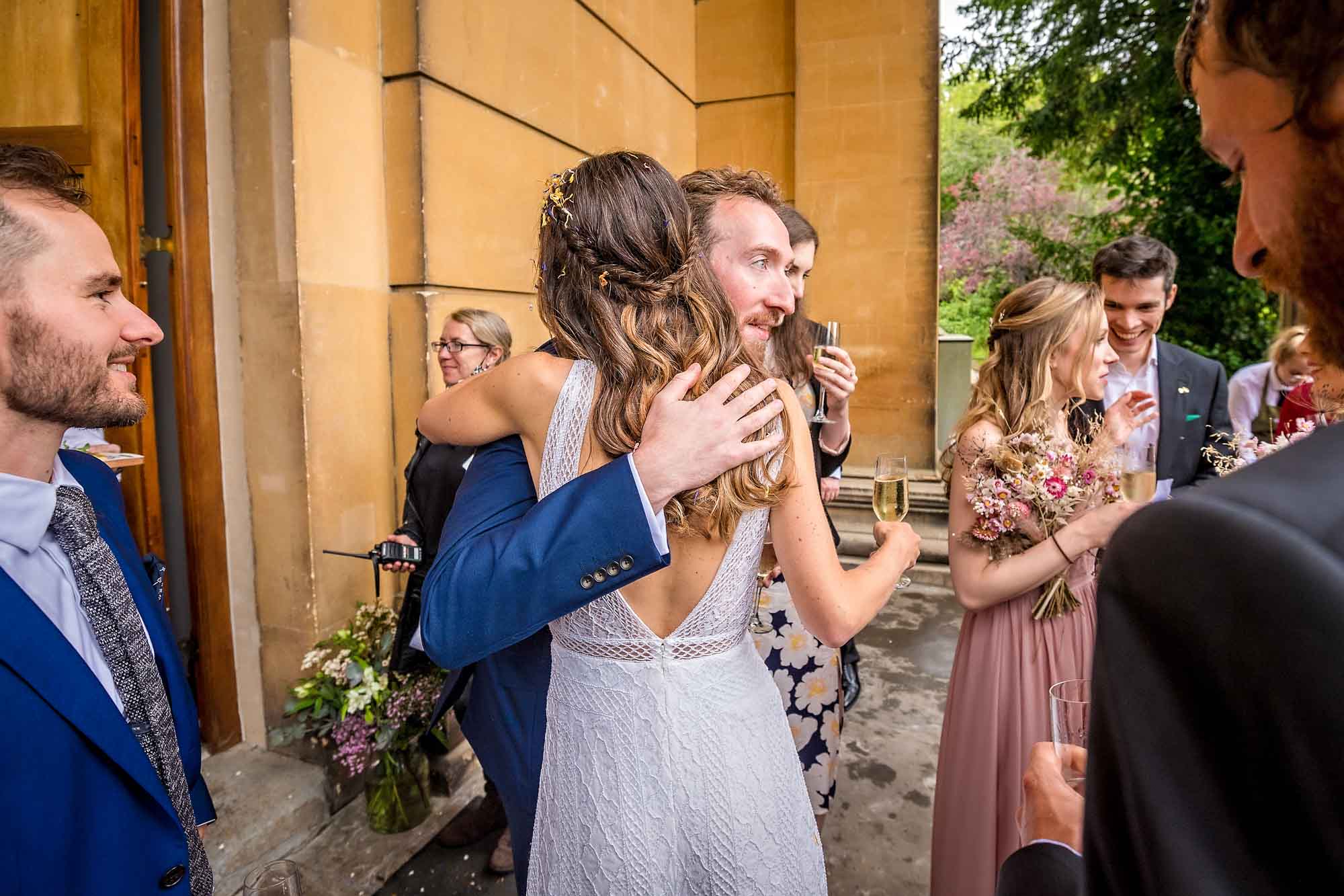 Male guest hugs bride as other mill around at wedding in Bristol
