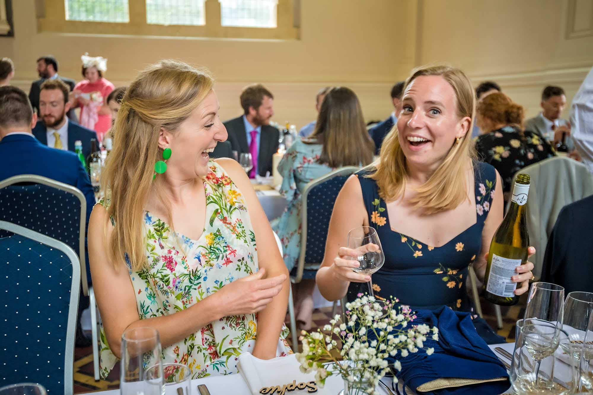Two women laughing with bottle of wine at wedding breakfast