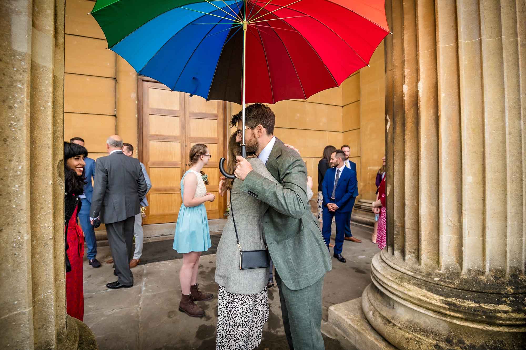 Groom hugging friend at Arnos Vale wedding holding colourful umbrella