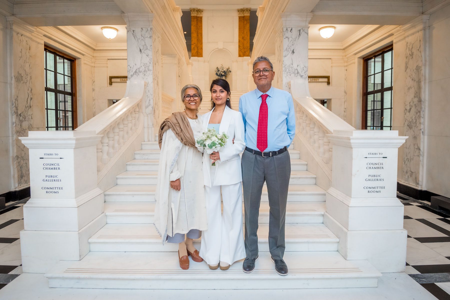 Asian bride poses with he parents at the foot of the Marble Staircase during her Camden Town Hall wedding