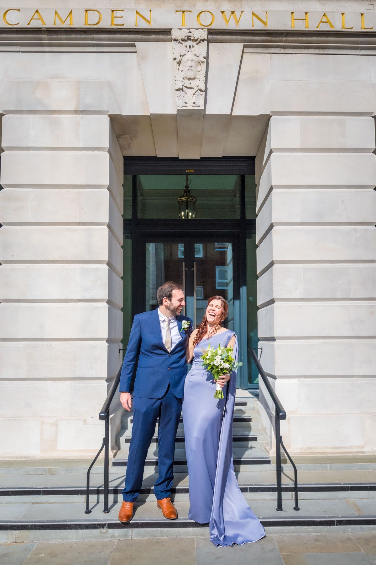 Bride in purple with her groom laughing outside Camden Town Hall after their wedding deremony