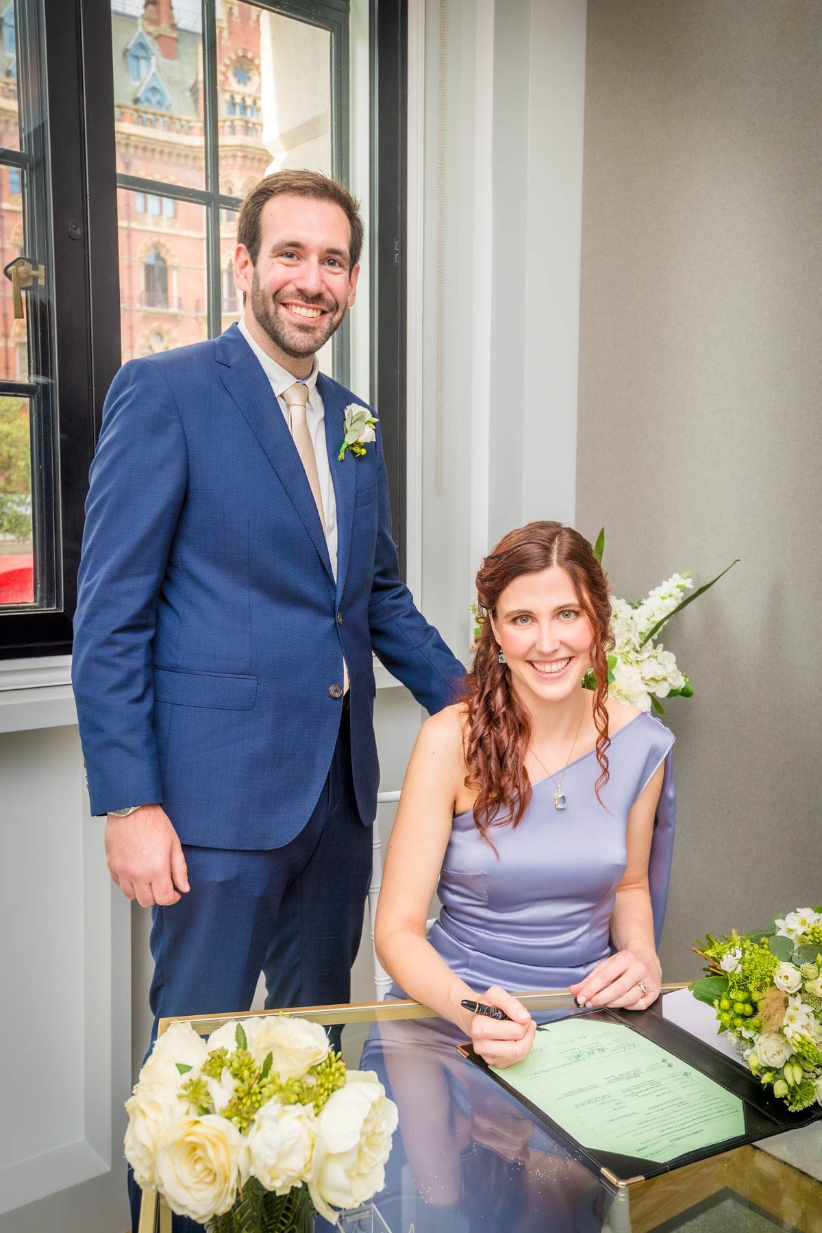 Bride holding signing pen with her groom as they smile for the camera