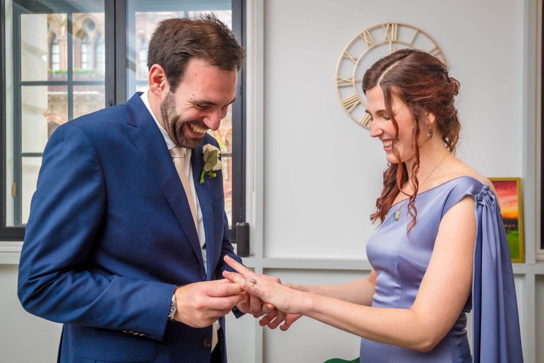 The bride and groom laughing as he tries to put a ring on her finger