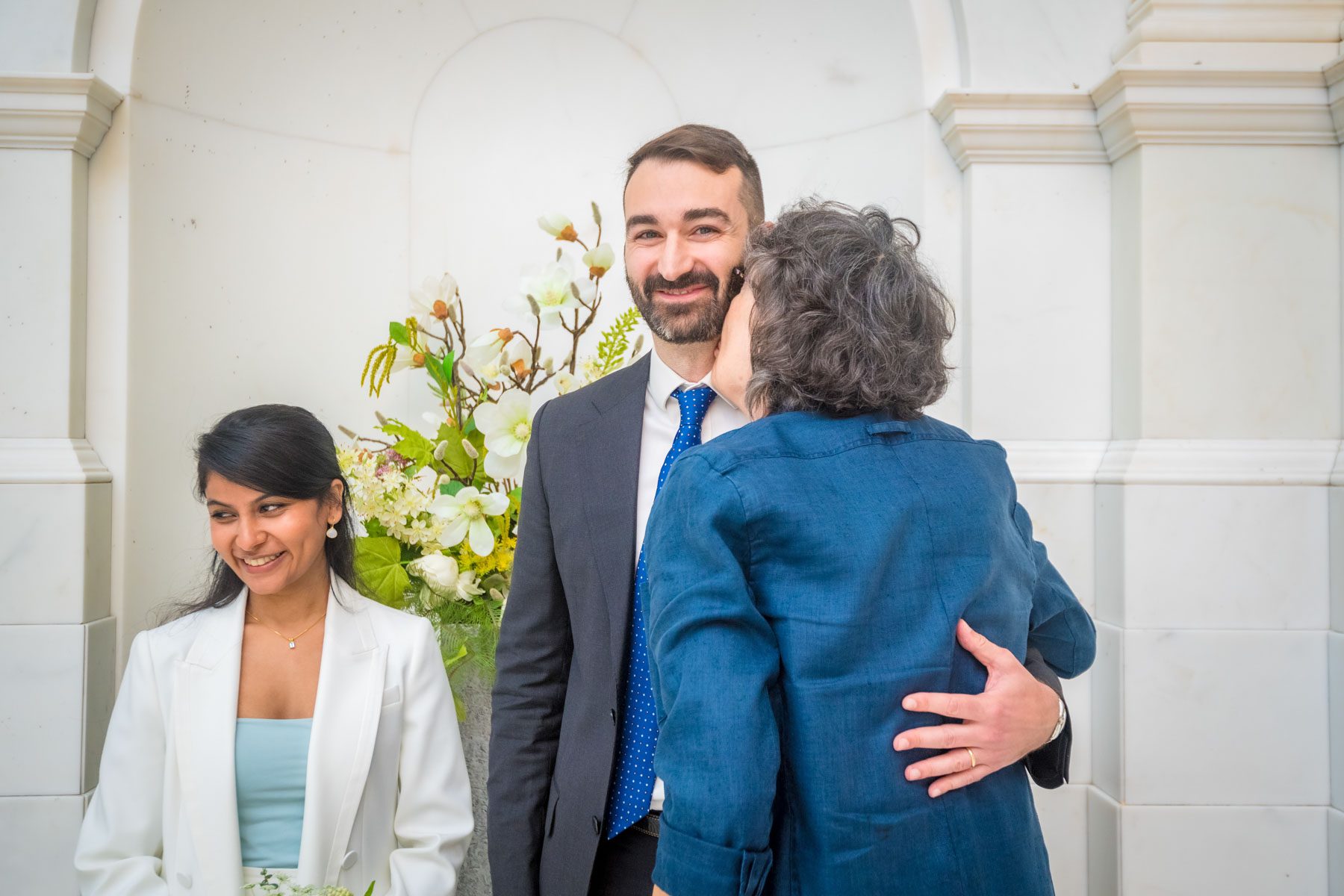 The groom grins as his mum kisses him on the cheek at a Camden Town Hall wedding