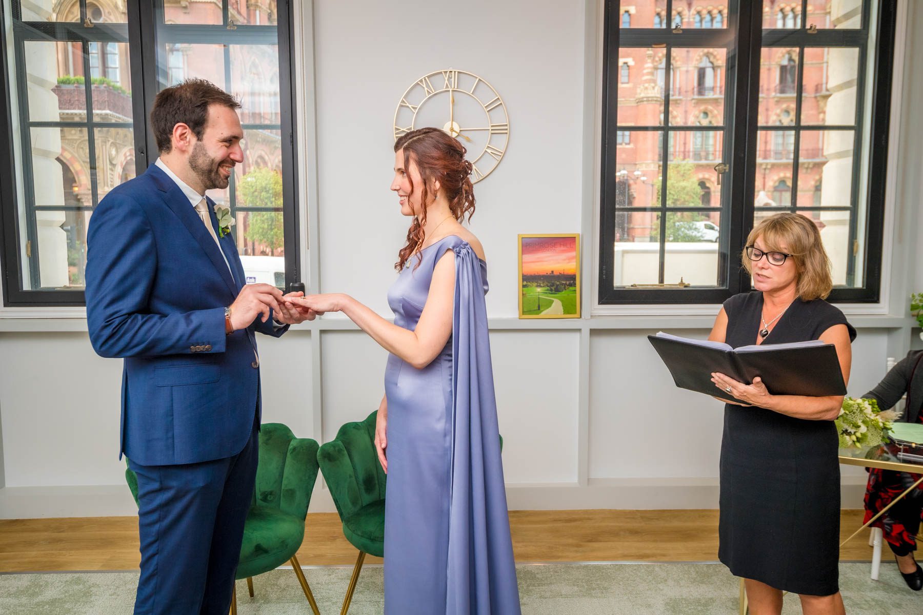 The bride and groom looking at each other whilst he places a ring on her finger and the registrar reads their vows