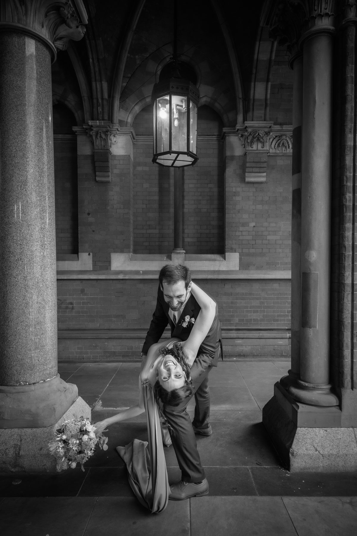 Black and white photo of wedding couple. Groom bending bride over backwards to look in the camera.