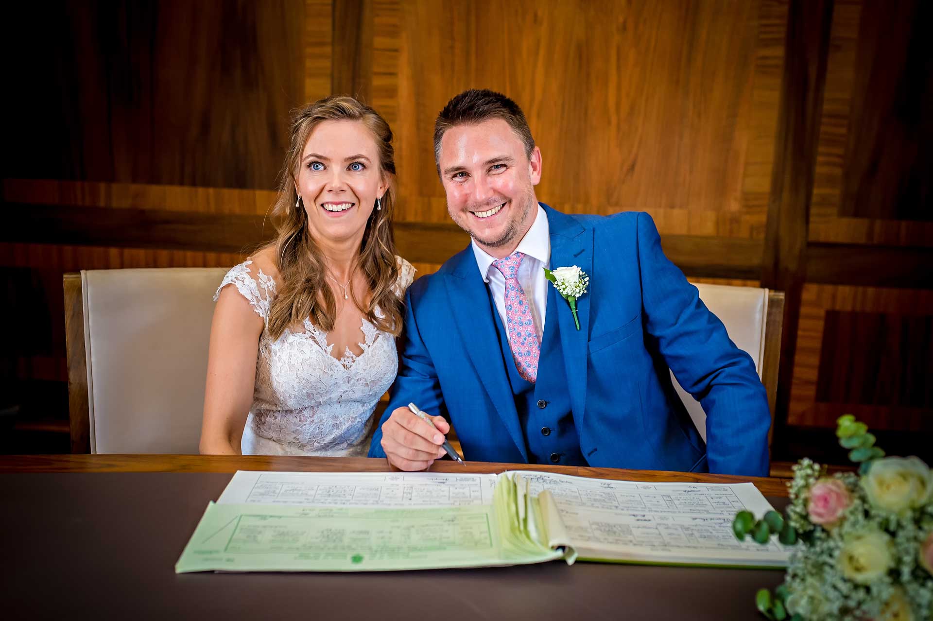 Groom signing dummy register with Bride - both grinning broadly