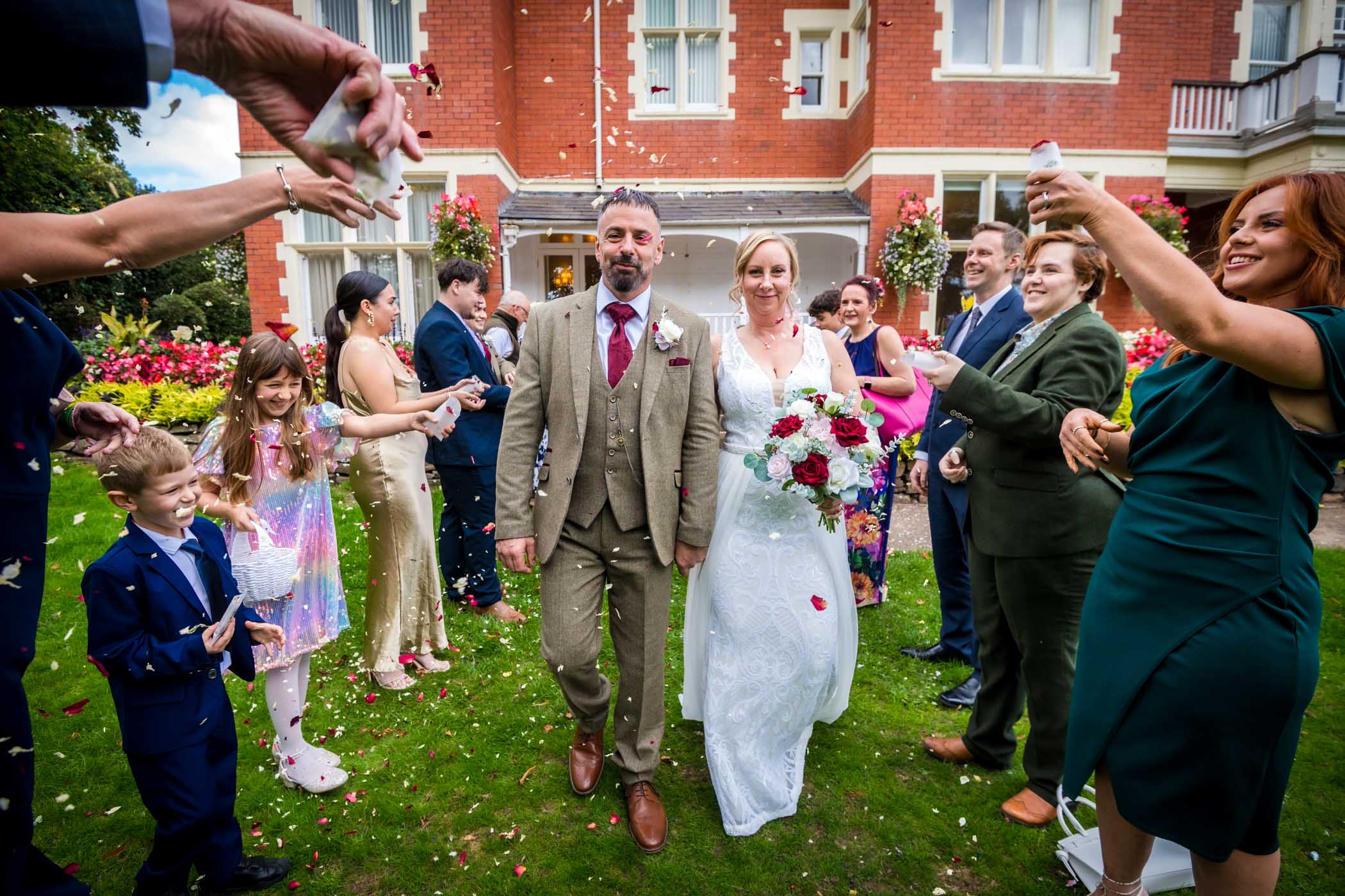 Couple walking through aisle of guests in gardens of the Mansion House in Newport whilst their guests throw confetti