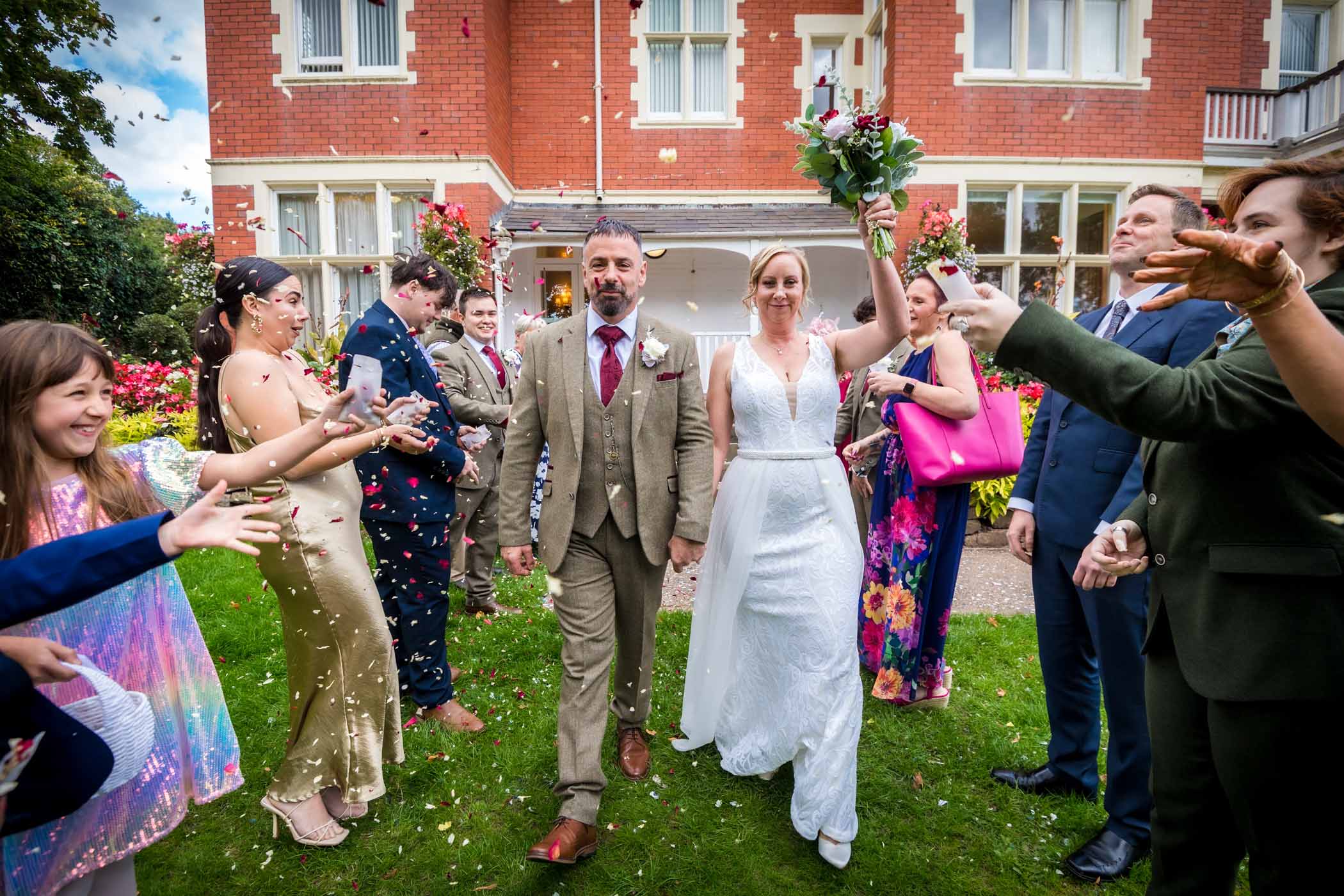 Couple walking through aisle of guests in garden of Newport Register Office whilst their guests throw confetti